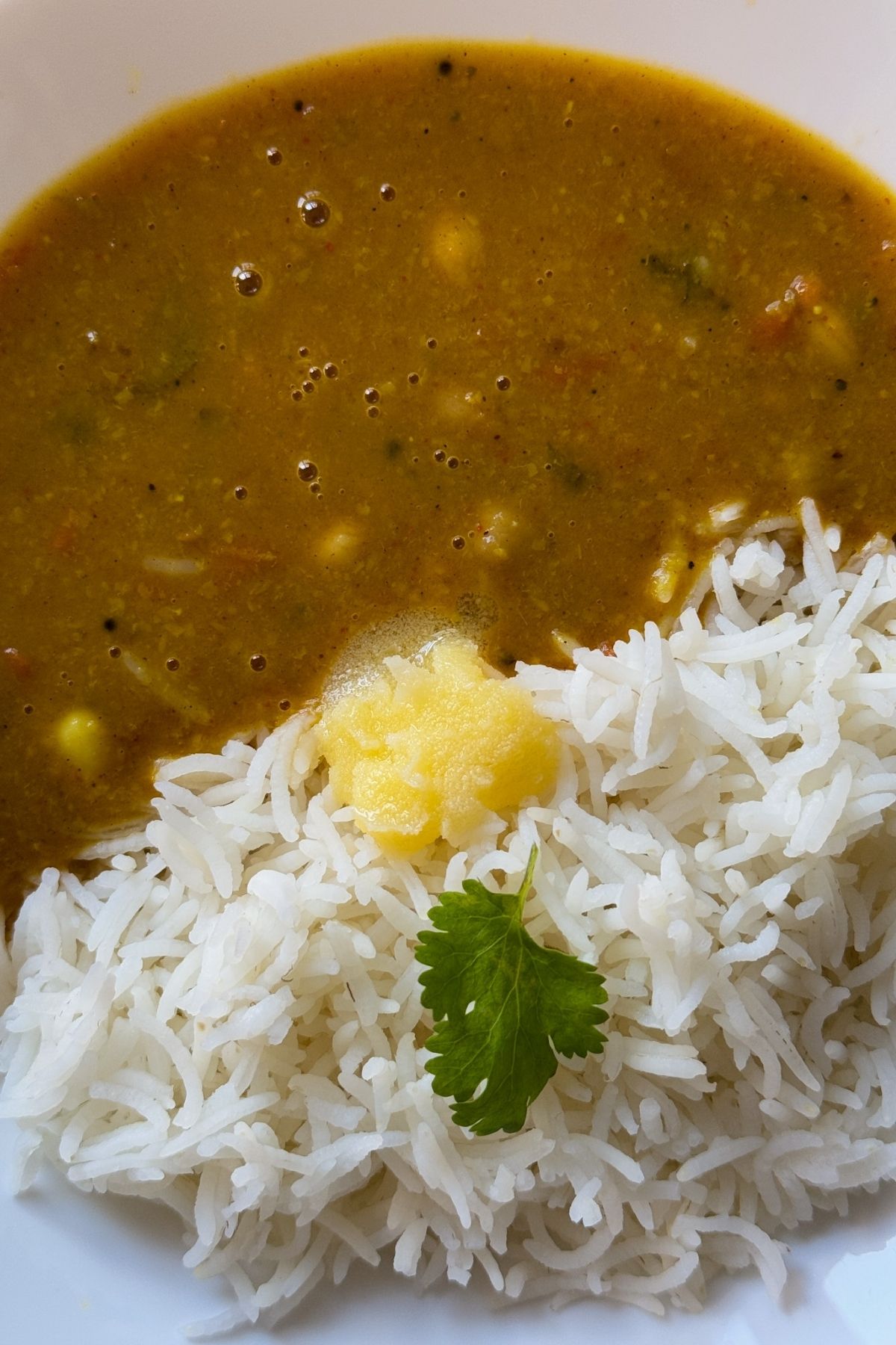 gujarati dal and rice with dollop of ghee in a white bowl.
