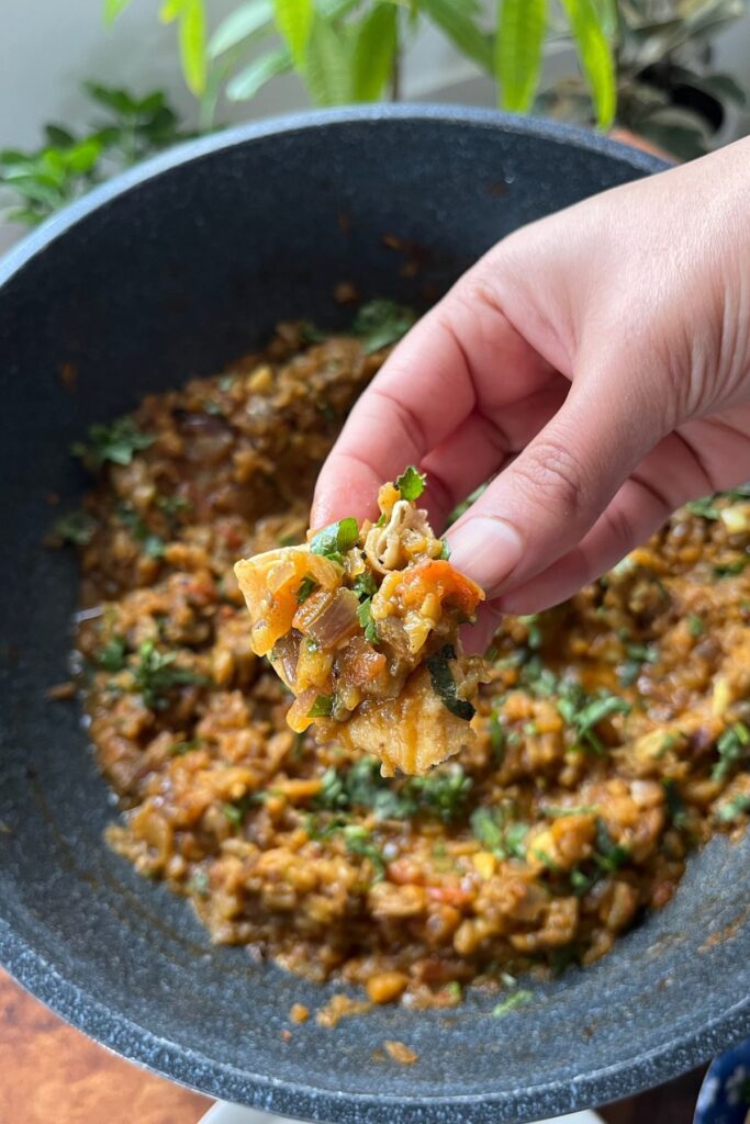 baingan bhartu with hands in a roti from a pan