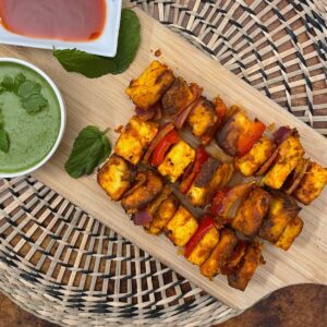 Paneer Tikka presented on a wooden board with a couple mint leaves served with green and red chutneys