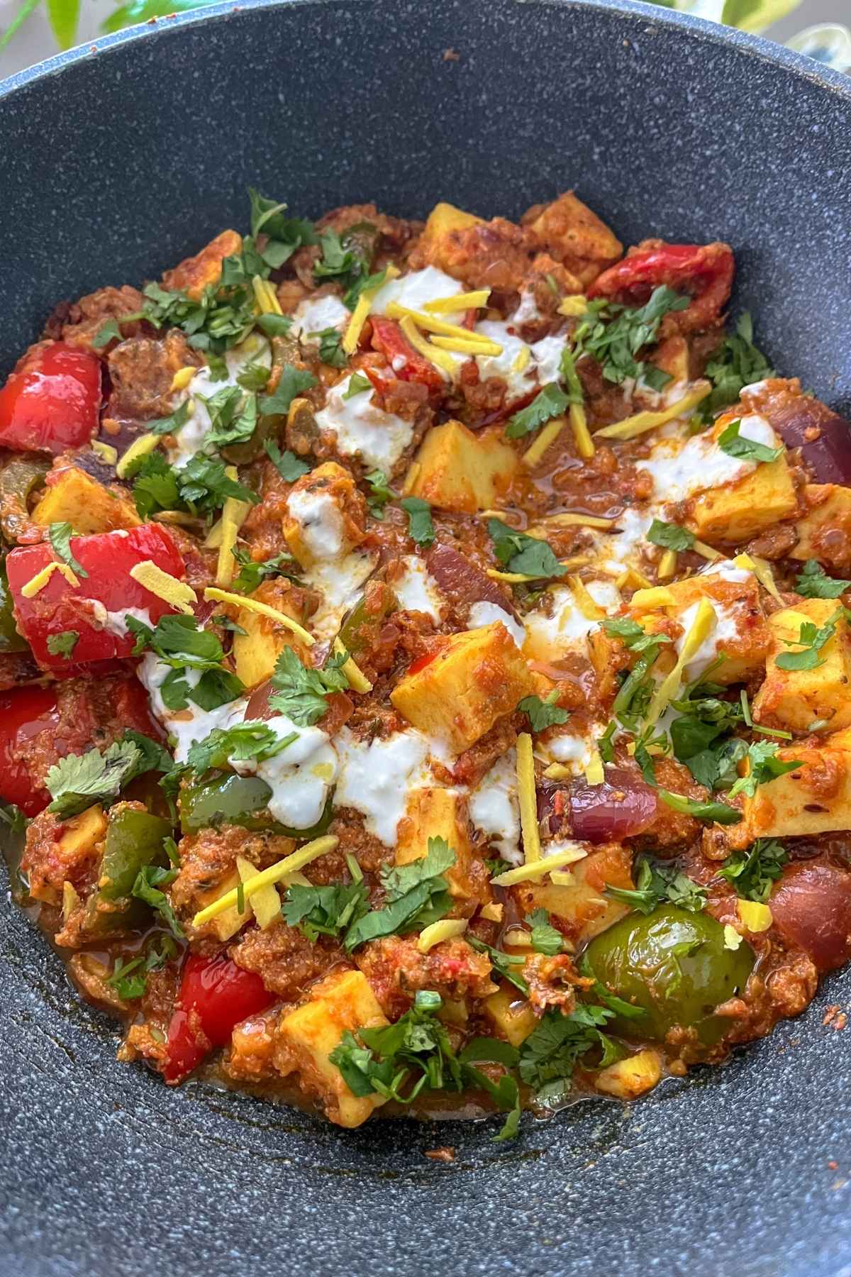 Prepared Kadai paneer in a wok with yogurt and ginger slices and garnished coriander.