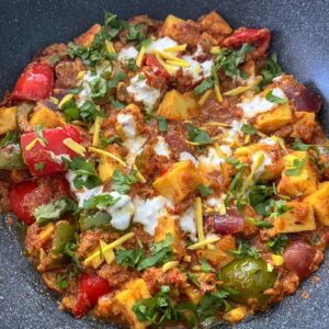 Prepared Kadai paneer in a wok with yogurt and ginger slices and garnished coriander.