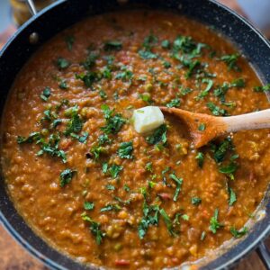 homemade mumbai street style pav bhaji in a pot with a cube of butter melting on the top and garnished cilantro.