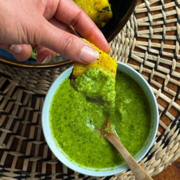 Dipping Khaman piece in a bowl of khaman chutney with a wooden spoon in it.