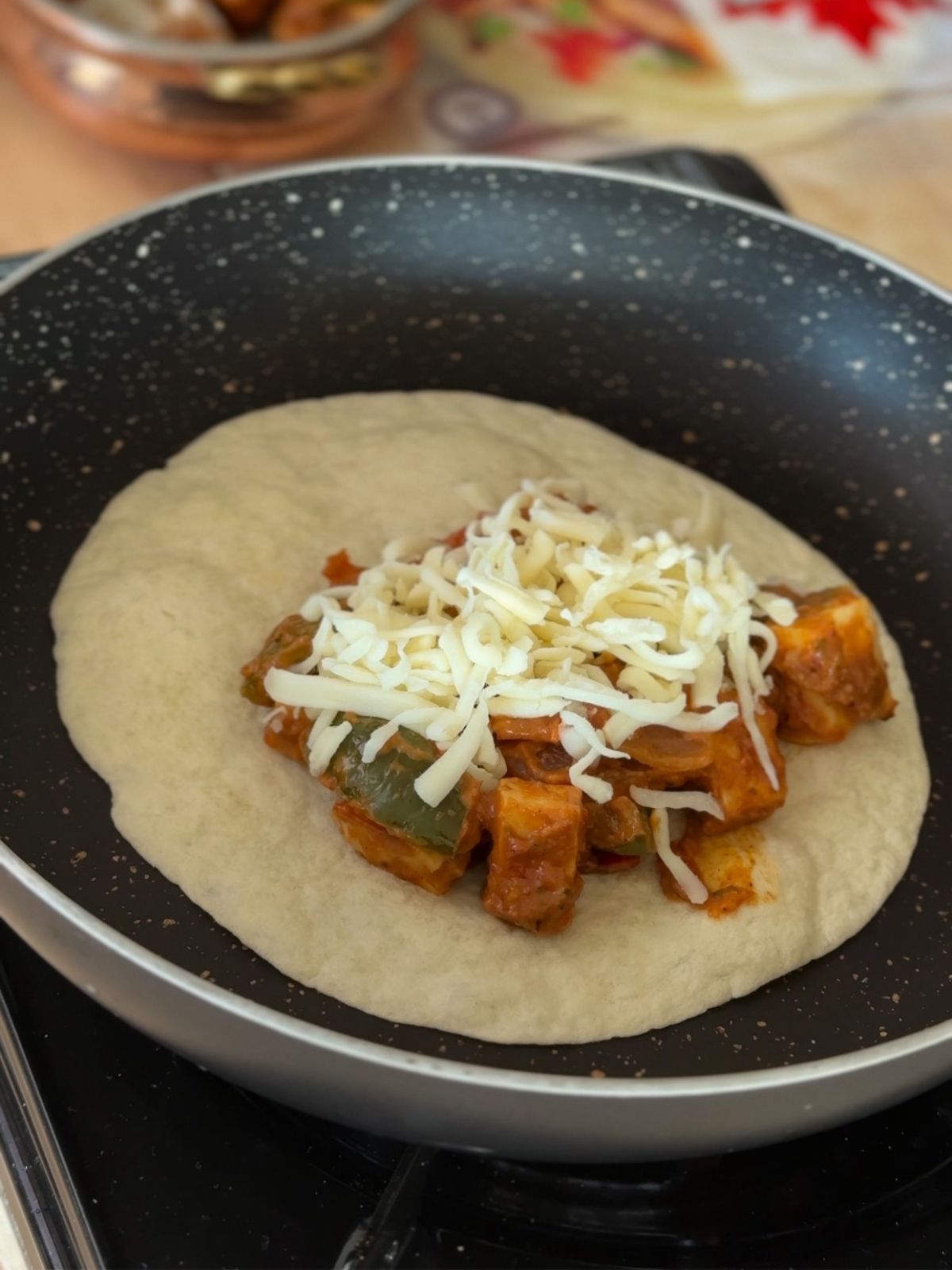 A flat tortilla in a black pan with tikka taco filling and cheese