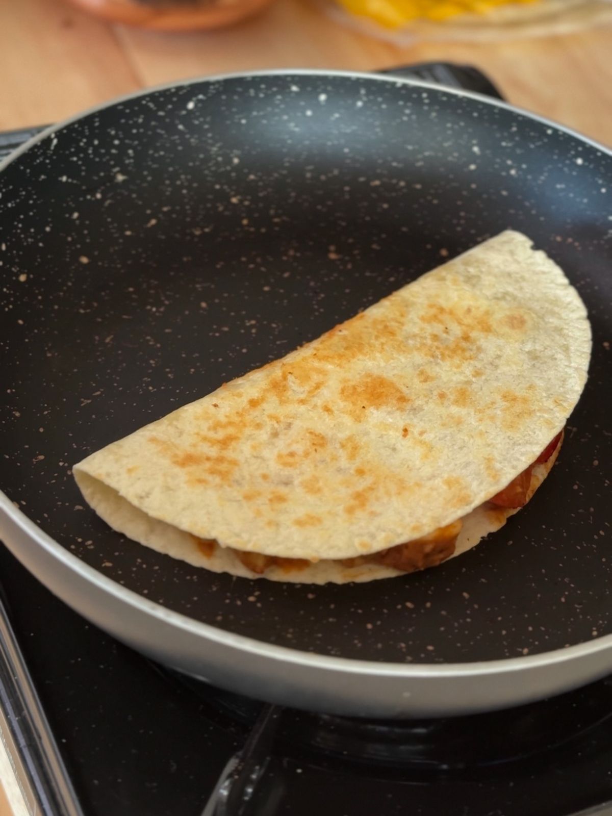 A folded tortilla cooked until brown on a black pan.