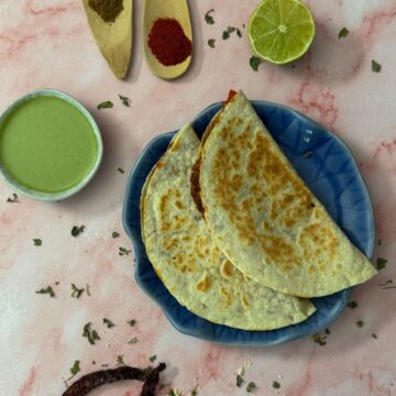 A plate with two tortillas presented with a green chutney, lime, and spices sprinkled around